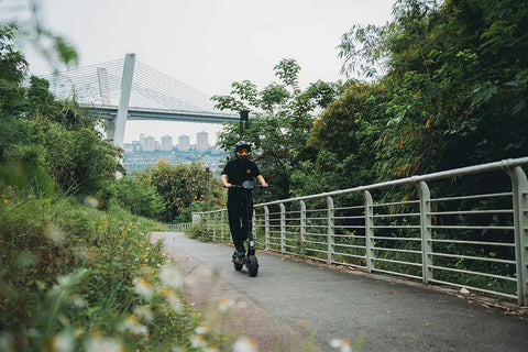 KuKirin G2 electric scooter cruising along a sun-dappled park trail, leisurely outdoor riding vibe
